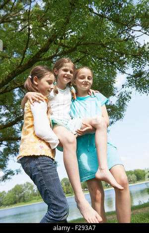 Zwei Mädchen, die Aufhebung ihrer Freundin am Seeufer, Bayern, Deutschland Stockfoto