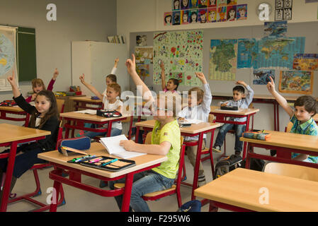 Schulkinder mit erhobenen Händen im Klassenzimmer, München, Bayern, Deutschland Stockfoto