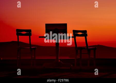 Einen leeren Tisch und Stühle, Baden in einem tiefroten Sonnenuntergang auf der Insel Santorini-Griechenland Stockfoto