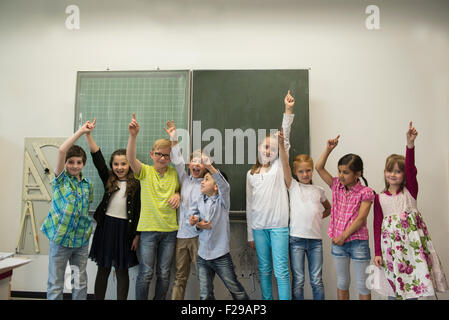 Schülerinnen und Schüler, die Hände vor der Tafel im Klassenzimmer heben, München, Bayern, Deutschland Stockfoto