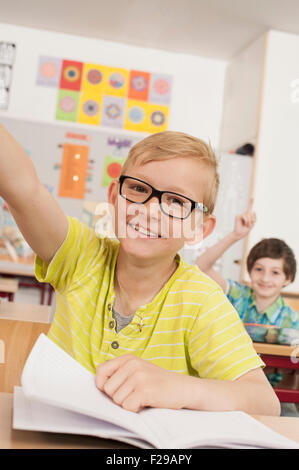 Schulkinder mit erhobenen Händen im Klassenzimmer, München, Bayern, Deutschland Stockfoto