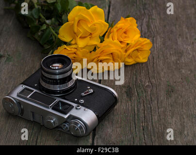 die alte Filmkamera und Bouquet von gelben Rosen auf einem hölzernen Hintergrund Stockfoto