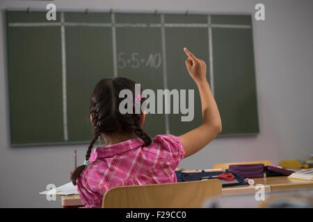 Schulmädchen vor der Tafel mit erhobener Hand im Klassenzimmer, München, Bayern, Deutschland Stockfoto