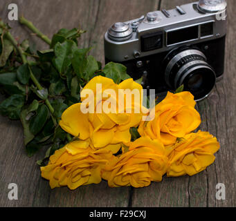 Bouquet von schönen gelben Rosen und die alte Kamera auf einem hölzernen Hintergrund Stockfoto