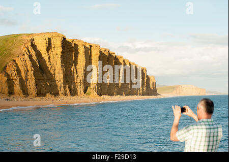 Mann mit dem Fotografieren von den Klippen der Jurassic Coast in der Nähe von West Bay, Bridport, Dorset, England, UK. Stockfoto