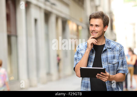 Glücklicher Mann hält eine Tablette und das Denken in der Straße Stockfoto