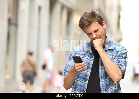 wütend zorniger Mann beobachtete apps auf dem Handy auf der Straße Stockfoto