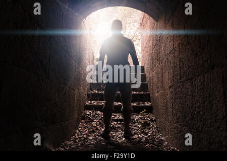 Junger Mann steht in dunklen Stein Tunnel mit glühenden Ende, warm getönten Foto mit Linse glow Effekt Stockfoto