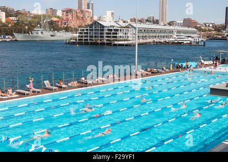 Sydney, Australien. September 2015. Büroangestellte kühlen sich mittags im Andrew Boy Charlton 50 Meter großen Freiluft-Swimmingpool an den Ufern der Woolloomooloo Bay ab, mit dem Wahrzeichen aus Holz im Hintergrund neben dem Marineschiff auf der Royal Australian Navy Garden Island Marinebasis, Sydney, NSW, Australien Stockfoto