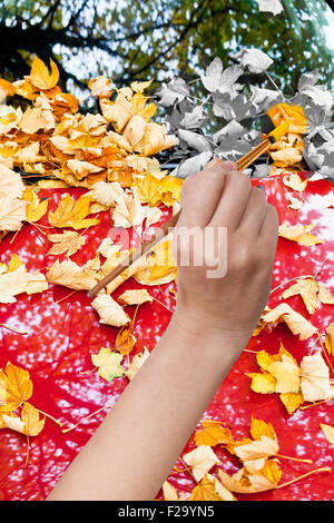 Natur-Konzept - Hand mit Pinsel malt gelbe Herbstlaub auf rotes Auto Stockfoto