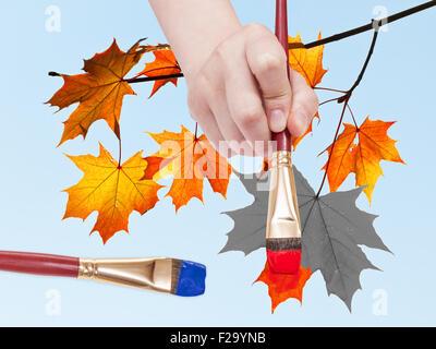 Natur-Konzept - Hand mit Pinsel malt Ahorn-Blätter in roter Farbe auf blauem Himmelshintergrund im Herbst Stockfoto