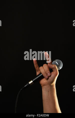 Männliche Hand mit Mikrofon mit Teufelshörnern Rock Blechschild auf schwarzem Hintergrund isoliert Stockfoto