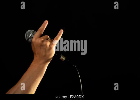 Männliche Hand mit Mikrofon mit Teufelshörnern Rock Blechschild auf schwarzem Hintergrund isoliert Stockfoto