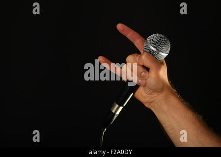 Männliche Hand mit Mikrofon mit Teufelshörnern Rock Blechschild auf schwarzem Hintergrund isoliert Stockfoto