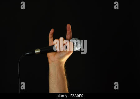 Männliche Hand mit Mikrofon mit Teufelshörnern Rock Blechschild auf schwarzem Hintergrund isoliert Stockfoto