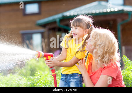 Kleine Gärtner-Mädchen mit Mutter Bewässerung auf Rasen in der Nähe von Haus Stockfoto