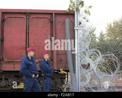 Roeszke, Ungarn. 15. Sep, 2015. Ungarische Polizisten bewachen das letzte Teilstück der Grenzzaun neben eines Güterwagens zwischen Ungarn und Serbien in der Nähe von Roeszke, Ungarn, 15. September 2015. Der Güterwagen wurde in Position Gefahren, um die Lücke im letzten Abschnitt der 175 Kilometer langer Zaun entlang der Grenze zwischen Serbien und Ungarn zu füllen. Foto: Thomas Brey, Dpa/Alamy Live News Stockfoto