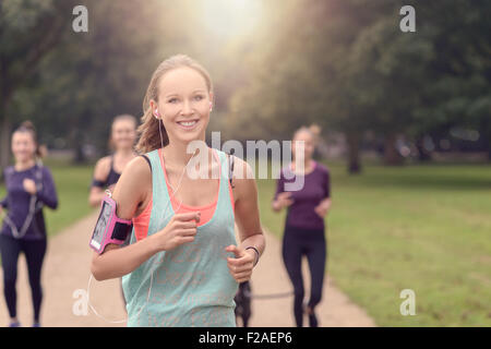 Eine halbe Stelle erschossen von ein Athletic ziemlich junge Frau lächelnd in die Kamera während Joggen im Park mit anderen Mädchen, mit Kopie spa Stockfoto