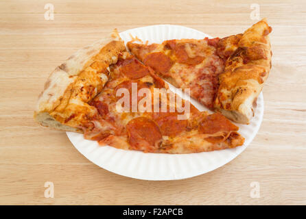 Zwei Scheiben frisch gebackene Peperoni-Pizza auf einem weißen Papierteller oben auf einer hölzernen Tischplatte mit natürlichem Licht beleuchtet. Stockfoto