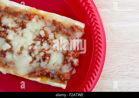 Enge Draufsicht von einem rechteckigen Stück gehackte Peperoni und Mozzarella-Käse-Pizza auf einer roten Platte oben auf einer hölzernen Tischplatte Stockfoto