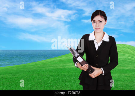 Geschäftsfrau hält Ordner Dokumente mit grünen Rasen Feld und Meer Hintergrund Stockfoto