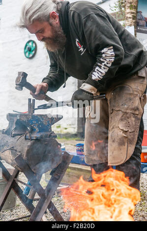 Ein Schmied hämmert ein Stück des Wrought Eisens auf einem Amboss. Stockfoto