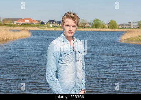 Schönen jungen Mann am Wasser stehen. Bluse tragen blaue und braune Hose Stockfoto