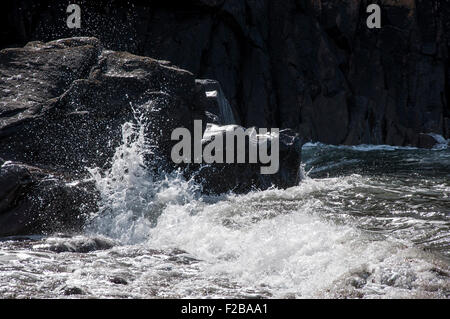 Wellen gegen Felsen an einem Strand in Pembrokeshire, Westwales. Sonnenlicht auf die Brandung. Stockfoto