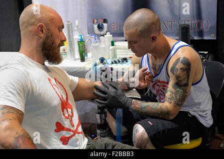 Garden City, New York, USA. 13. September 2015. LUKE PALAN, ein Tattoo-Künstler aus Las Vegas, ist ein Mann Arm auf der United Tinte Flug 915 Tattoo Convention im Cradle Aviation Museum in Long Island tätowieren. Der bärtige Mann ist ein Psycho-Hase weißen und roten t-Shirt. Bildnachweis: Ann E Parry/Alamy Live-Nachrichten Stockfoto