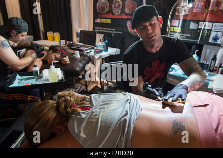 Garden City, New York, USA. 13. September 2015. R-L, JASON ACKERMAN und TROY RADECKI, ein Profi-Team von Tattoo-Künstler, sind zwei junge Frau, Bauchlage, auf der United Tinte Flug 915 Tattoo Convention im Cradle Aviation Museum in Long Island tätowieren. Bildnachweis: Ann E Parry/Alamy Live-Nachrichten Stockfoto