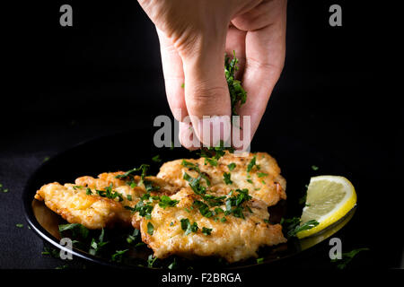 Gebratenes Hähnchenschnitzel mit Zitrone und Petersilie hinzufügen Stockfoto