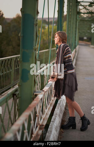 Modisches Teenagers Mädchen lehnte sich gegen das Geländer einer Brücke in Stiefel, Kleid und ein Pullover gekleidet. Stockfoto