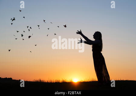 Teenager-Mädchen werfen Origami Schmetterlinge in der Luft bei Sonnenuntergang. Silhouette Stockfoto