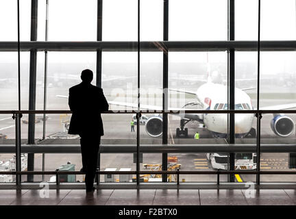 London, UK - 14. August 2015: Silhouette eines Reisenden warten auf ein Flugzeug in der Abflughalle Heathrow Flughafen an einem regnerischen Tag Stockfoto