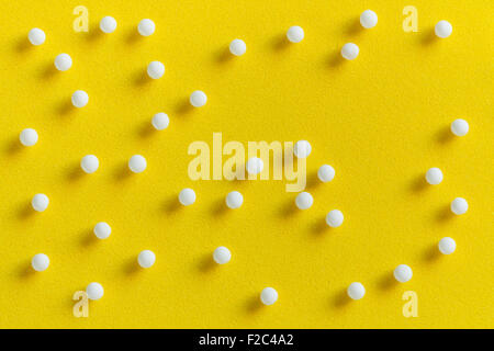 Draufsicht auf homöopathische Pillen (hergestellt aus inerten Material - Zucker/Lactose) auf eine gelbe Fläche verstreut. Stockfoto