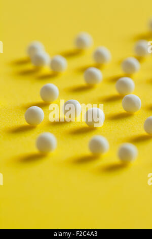 Makro Nahaufnahme homöopathische Pillen (hergestellt aus inerten Material - Zucker/Lactose) auf eine gelbe Fläche verstreut. Stockfoto