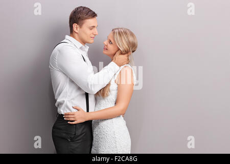 Elegante Mann, hält eine Mädchen am Hals zu küssen gegen eine graue Wand Stockfoto