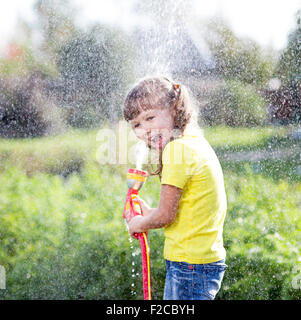Fröhliches Kind Bewässerung von Pflanzen aus Schlauch Spray im Garten im Hinterhof des Hauses am sonnigen Sommer Stockfoto