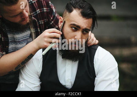 Barbier rasiert ein bärtigen Mannes Stockfoto
