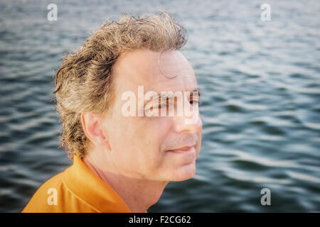 Edel 40 Jahre alten Sportler mit drei-Tage-Bart und Salz und Pfeffer Haar trägt eine orange Polo-Shirt, während er, direkt am Meer denkt Stockfoto