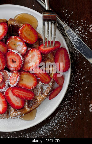 Draufsicht auf eine Waffel mit Erdbeeren, Puderzucker, Zucker und Sirup auf weißen Teller Stockfoto