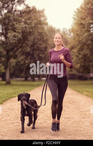 Voller Länge Schuss eine gesunde junge Frau Joggen im Park mit ihrer schwarzen Hund Stockfoto