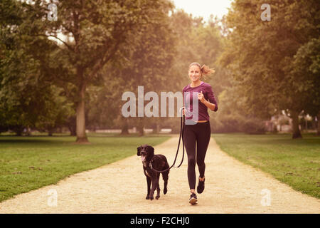 Voller Länge Schuss eine gesunde junge Frau Joggen im Park mit ihrer schwarzen Hund Stockfoto