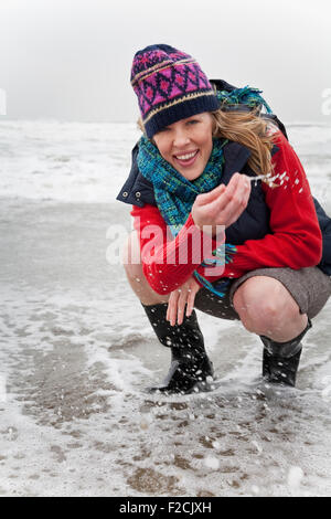 Junge Frau hockt im Ozean tragen Winterkleidung Stockfoto