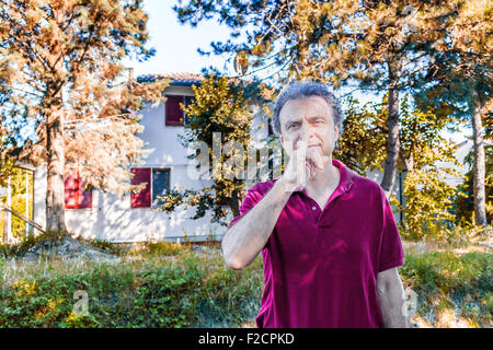 Charismatisch und schön kaukasischen Sportler von vierzig mit grauen Haaren, die in rote Polo Hemd und dunkle Leinenhosen lädt Sie ruhig mit einem Finger über seine Lippen in einem Park in der Emilia Romagna in Italien zu sein Stockfoto