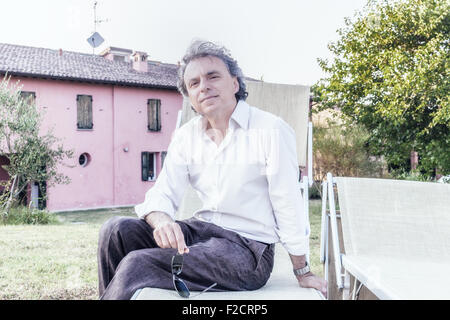 faszinierende wohlhabenden Gentleman von vierzig aus Stadt ruht auf einem Liegestuhl im Garten von einem roten Landhaus in Italien Stockfoto