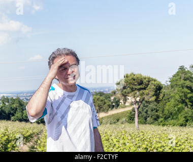 Gut aussehend 40 Jahre alter Mann mit Salz Pfeffer Haar gekleidet mit Sport-Shirt hält seinen Kopf in den Feldern der italienischen Landschaft: er scheint Kopfschmerzen haben Stockfoto