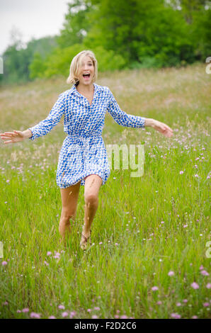 Mädchen mit blonden Haar läuft durch Feld im blauen Kleid beim Lachen und winken ihr Arme Stockfoto