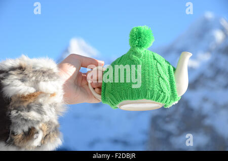 Teekanne in der geknoteten Kappe in der Hand gegen die alpine Landschaft Stockfoto