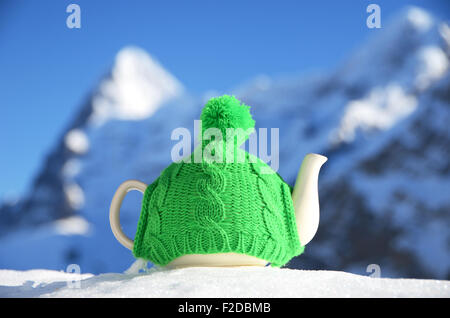 Teekanne in die Strickmütze auf dem Schnee gegen Berggipfel Stockfoto